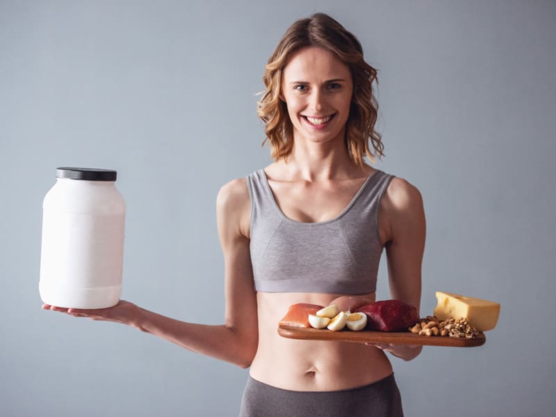 LM-pros-of-protein1 woman holding good protein food and also protein powder to illustrate protein intake needs