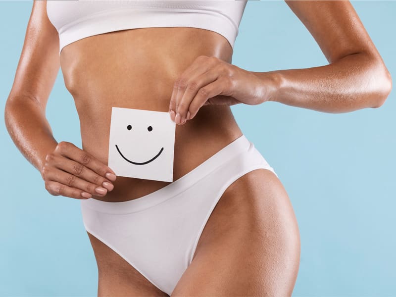LM-Emsculpt-Neo Woman holding paper smiley in front of her toned body to illustrate the benefits of Emsculpt Neo treatment