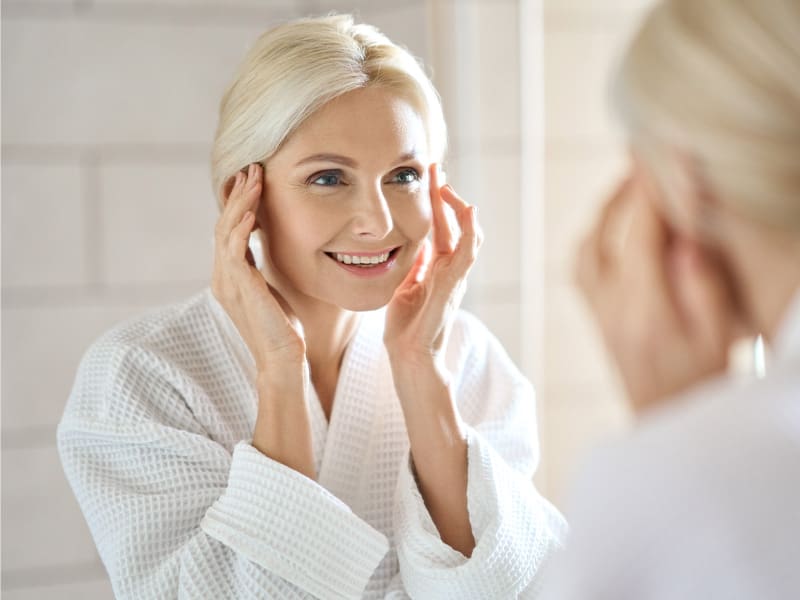 LM-anti-aging-Niagen-IV-therapy woman with glowing skin looking happily in the mirror - to illustrate the effects of Niagen IV therapy