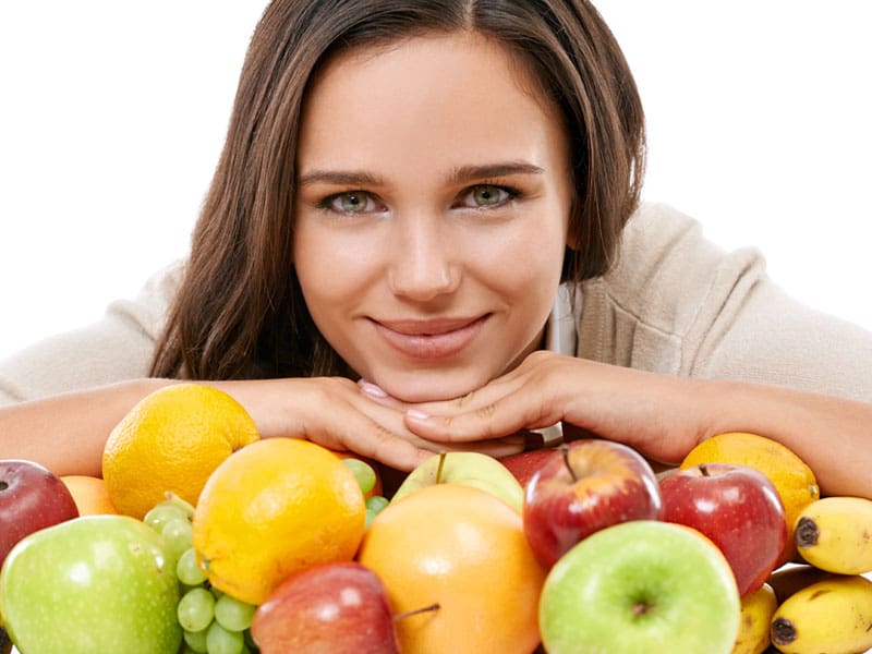 LM-best-foods-for-your-skin Smiling woman with glowing skin and an array of healthy fruit to illustrate best foods for your skin