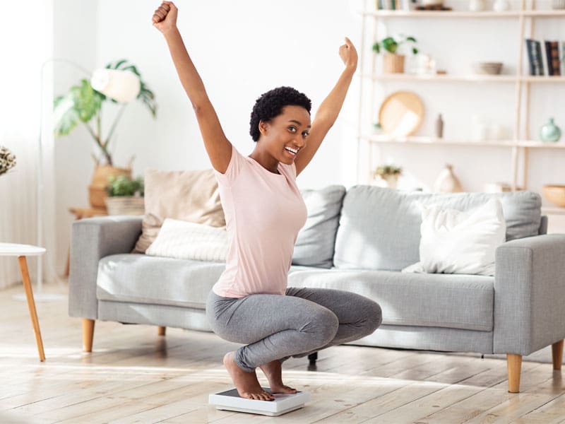 LM-semaglutide-and-weight-loss main image young woman sitting on scales with arms raised to illustrate the success of semaglutide and weight loss