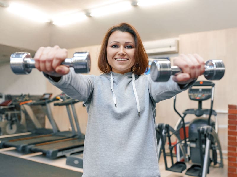LM-does-perimenopause-cause-weight-gain woman in gym using hand weights to illustrate does perimenopause cause weight gain