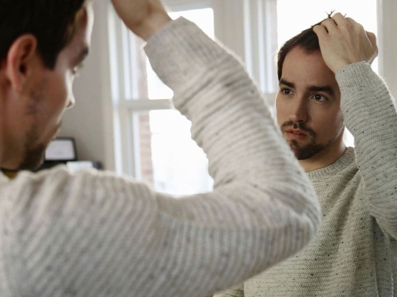 LM-what-is-PRP-for-hair Man inspecting hair in mirror to illustrate thinking about PRP for hair loss